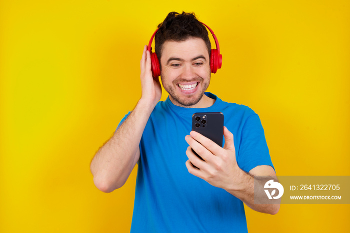 Joyous young handsome caucasian man wearing blue t-shirt poses with mobile phone device, types text 