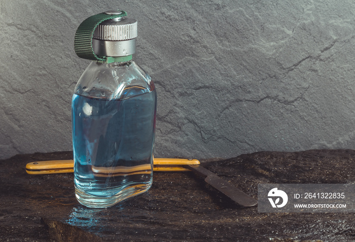 Clear blue aftershave bottle with old razor on wet stone