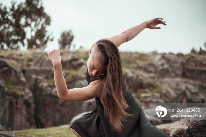 Hipster female with long hair practicing contemporary dance against sky