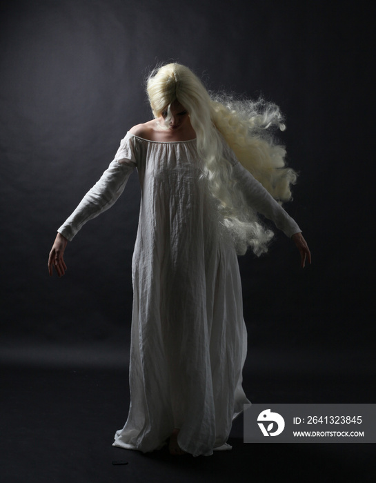 一位身穿白色长袍的金发女子的幽灵般的全身肖像。站着摆出一个姿势