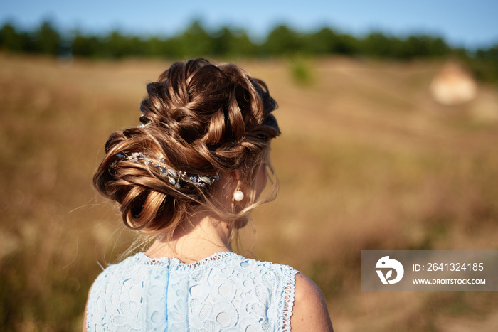 Beautiful bride wedding hairstyle with jewelry, back view. Girl with curly hair styling outdoors. Ha