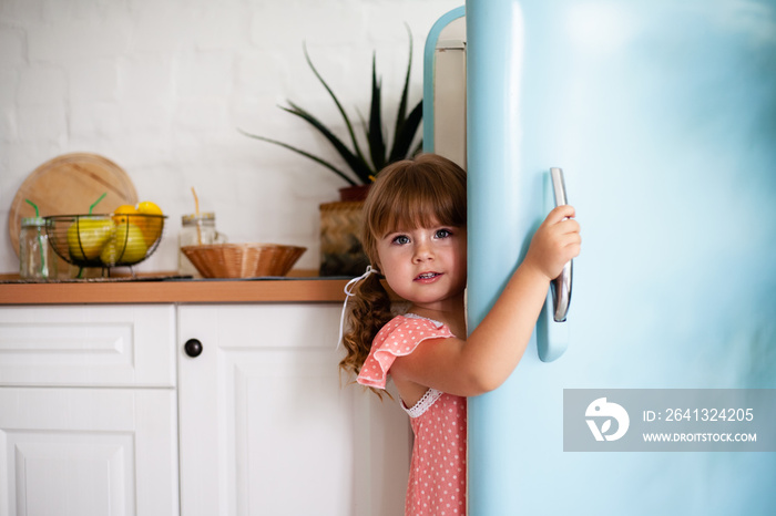 一个小女孩打开冰箱的门。漂亮的厨房。