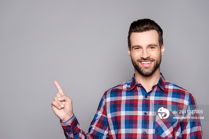 A portrait of a young happy smiling man in checkered shirt isolated on gray background poiting on co