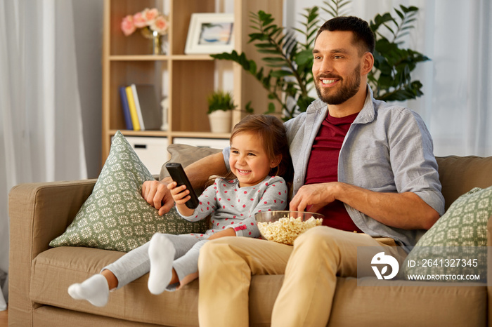 family, fatherhood and people concept - happy father and daughter with popcorn and remote control wa