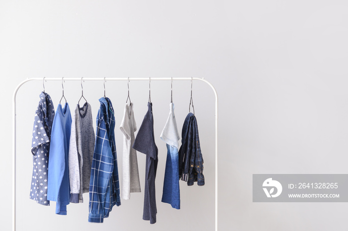 Stylish kid clothes hanging on rack against light background