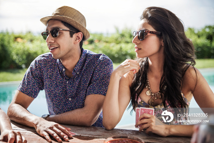 Young couple playing cards at poolside table