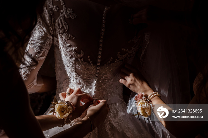 Bridesmaid helping bride fasten corset and getting her dress, preparing bride in morning for the wed