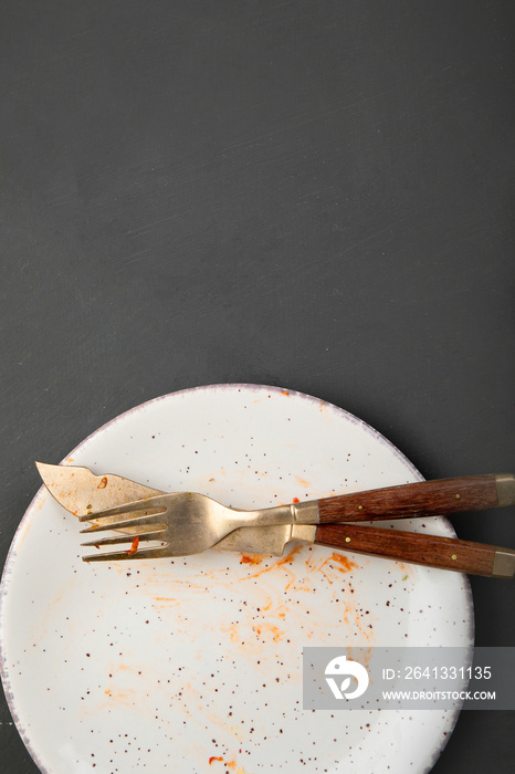 Pile of empty and dirty plates with food leftovers on dark background.