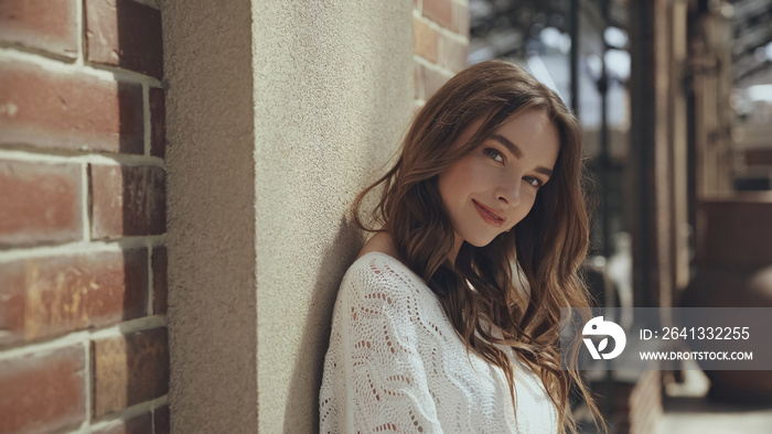 smiling young woman looking at camera near building outside.