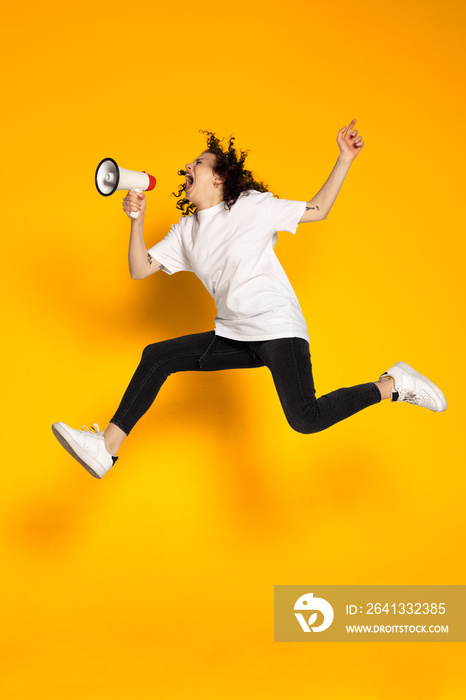 Full-length portrait of young cheerful girl, student in white t-shirt and jeans jumping isolated on 