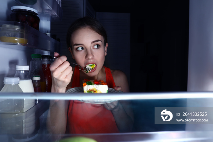 一个在冰箱附近吃东西的年轻女人，从里面看