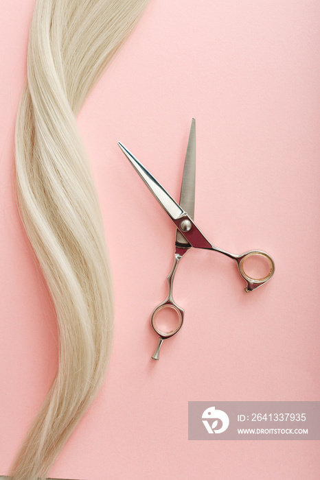 Flat lay composition with Hairdresser tools - scissors and strand of blonde hair on pink color backg