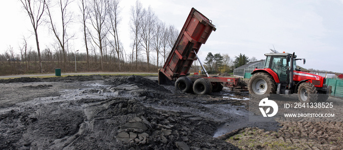 Tractor with tipper trailer dumping dredging spoil on a field