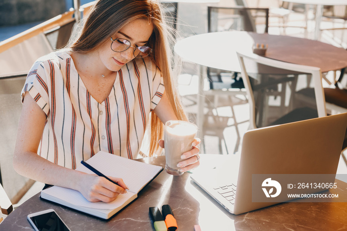 Upper side photo of a nice girl who is working in a copybook , sitting at the computer with a cup of