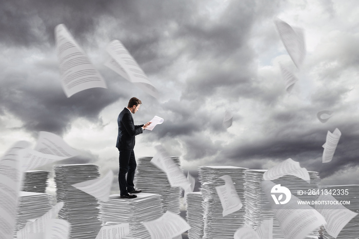 Businessman at work over a pile of paper towers of worksheets