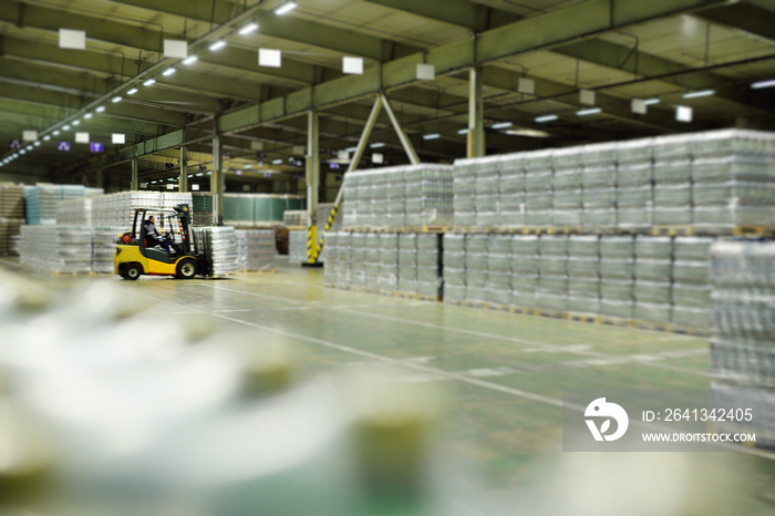 Yellow loader on the background of a huge industrial food warehouse with plastic PET bottles with be