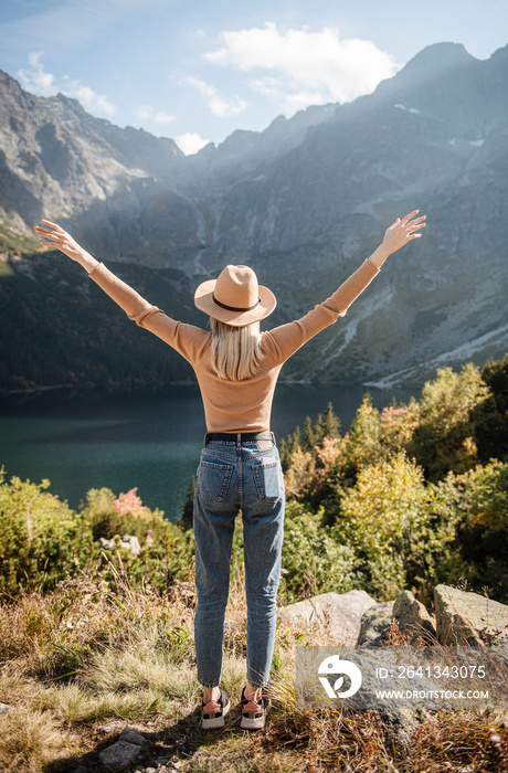 Young tourist woman in a hat with hands up on the top of the mountains