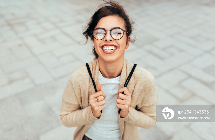 Outdoors horizontal portrait of young woman smiling broadly with toothy smile, with backpack on the 