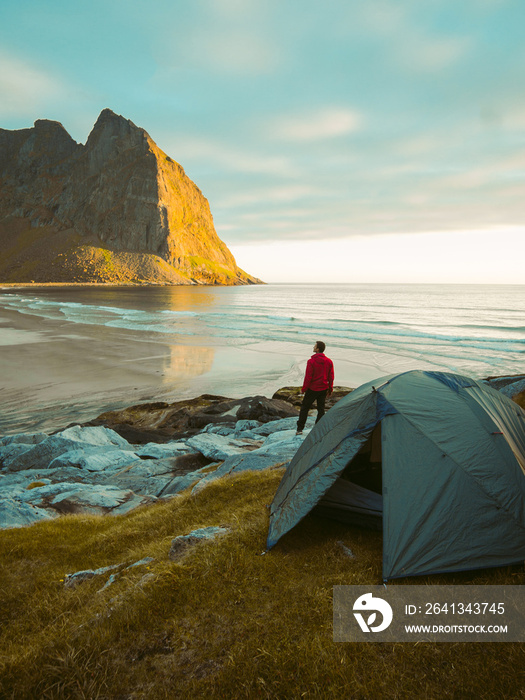 一个冒险的男人站在帐篷旁边的海滩上，欣赏着一场v形运动中的美景