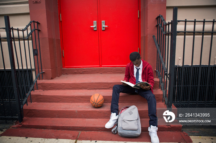 Boy sitting on steps and reading book outdoor