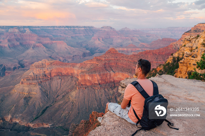 Young man sitting by the edge of the Grand Canyon exploring the view around him during sunset time. 