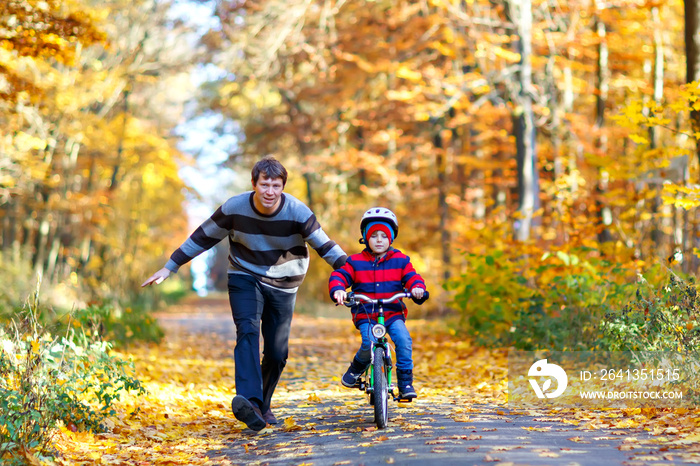 一个小男孩和他的父亲在秋天的公园里骑着自行车。爸爸在教儿子骑自行车