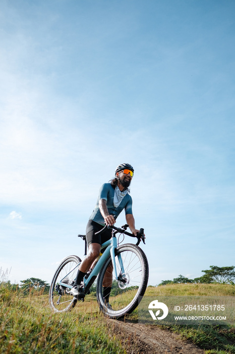 A young bearded cyclist is biking through a field