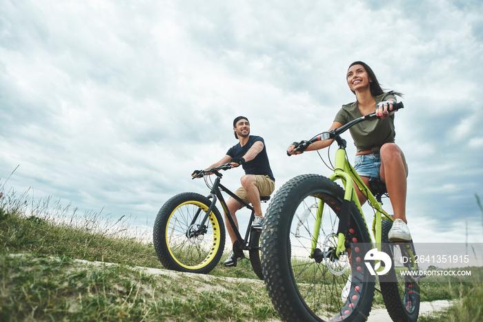 Young couple are cyclingat green hills . Front view