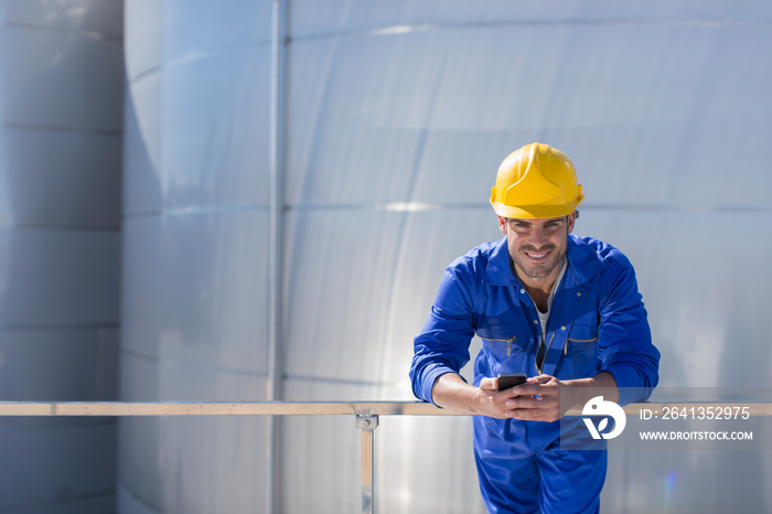 Portrait smiling male worker with smart phone in hard hat and coveralls