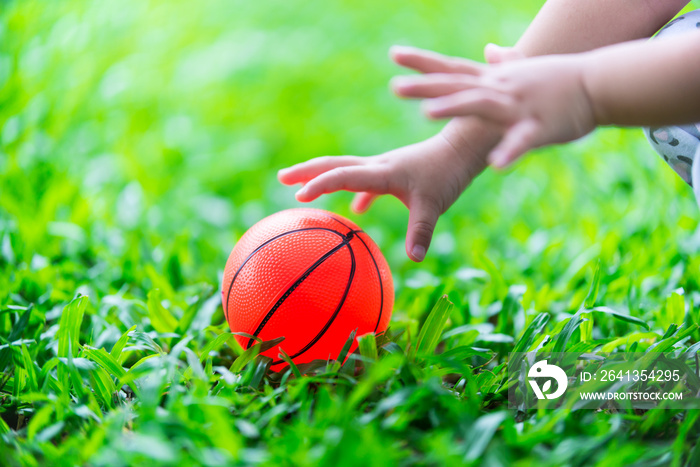 The ball is on the green lawn. Two small childrens hands are reaching for the ball.