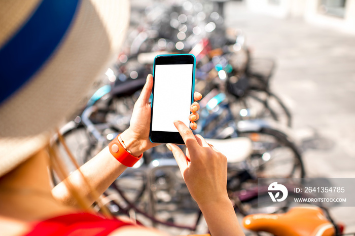 Woman holding smart phone with white screen on the bicycle parking background. Bicycle rent with sma