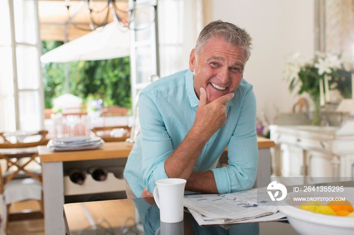 Portrait happy senior man drinking coffee and reading newspaper in kitchen