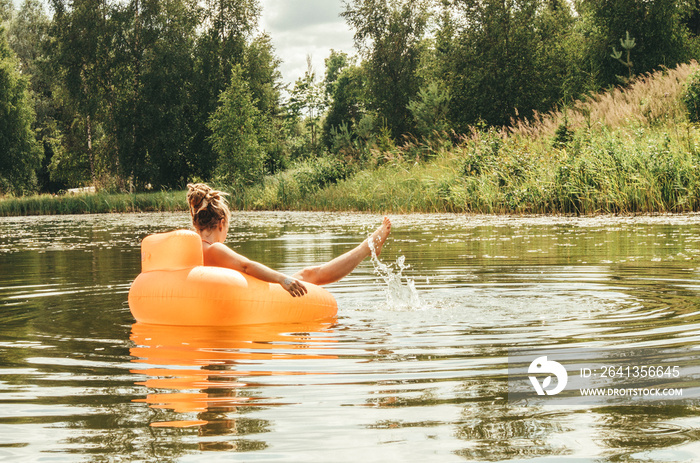 Young adult woman having fun, resting and sunbathing, relaxing on inflatable round orange chair toy 