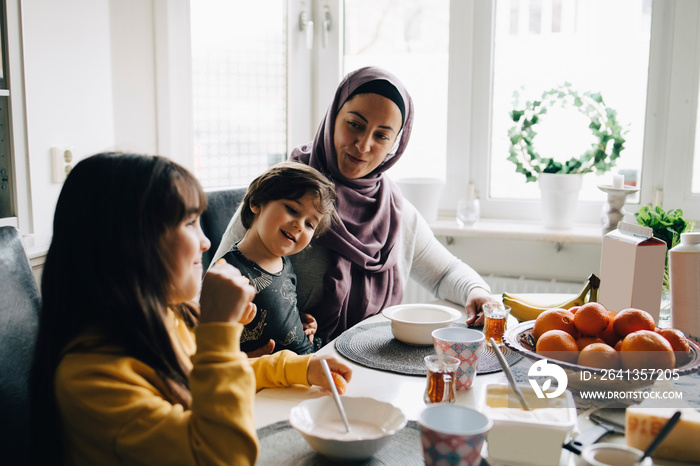 Smiling mother talking to children while having breakfast at dining table