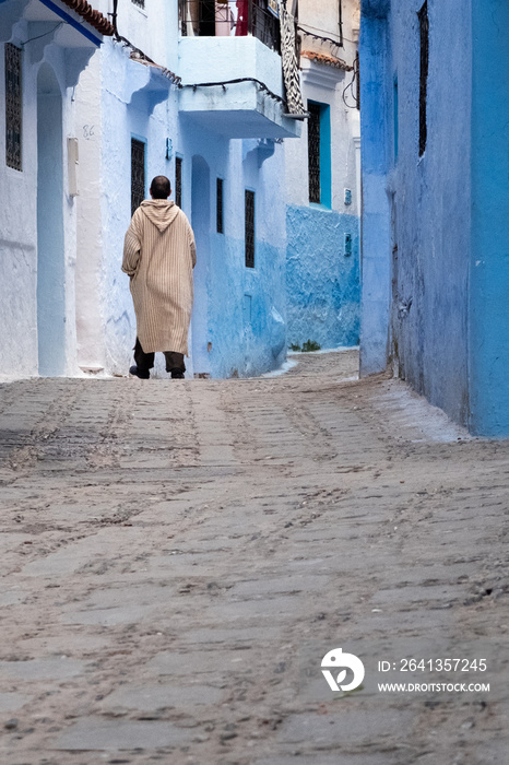 In the medina of Chefchaouen in Morocco. A man wearing the traditional Berber coat walks down a stre