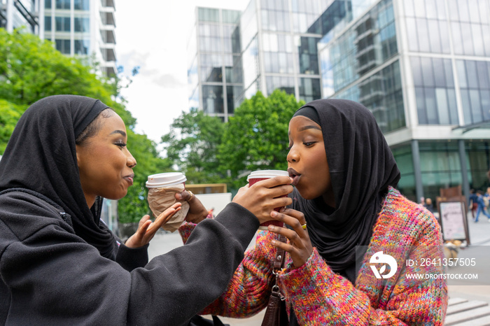 Young women wearing hijabs sharing coffee in city