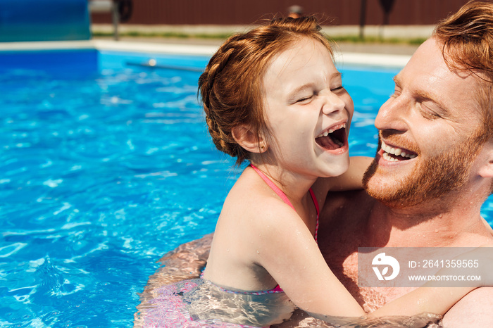 大笑的父亲在游泳池里拥抱微笑的小女儿