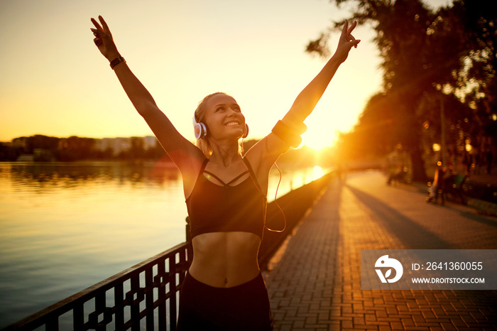 健康生活方式的概念。日落时，戴着耳机的女孩在公园里跑步。