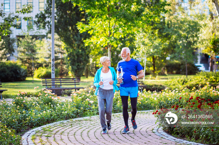 Happy senior couple jogging outdoors in park.