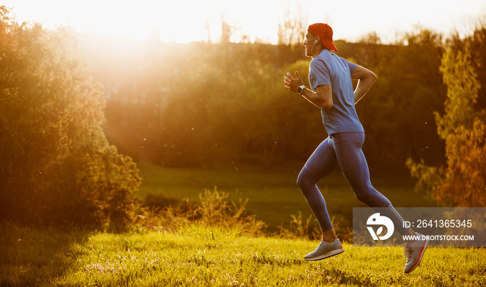 Fit young male jogger exercising in the park on sunset sunlight. Handosme athlete runner running and