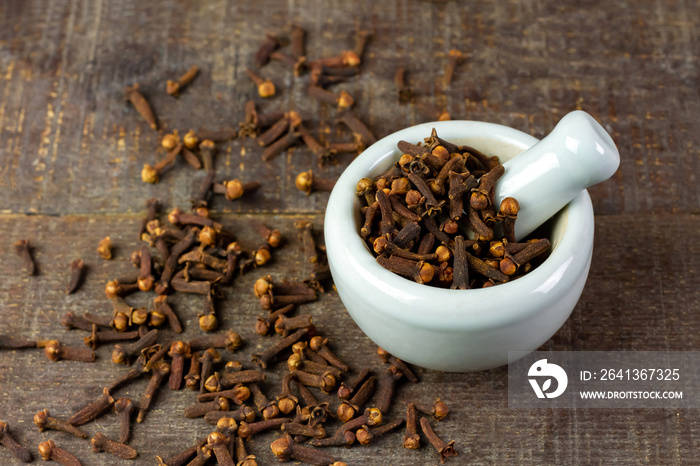 Cloves in white mortar with pestle on rustic wooden background. Herbal cloves have a fragrant and sp