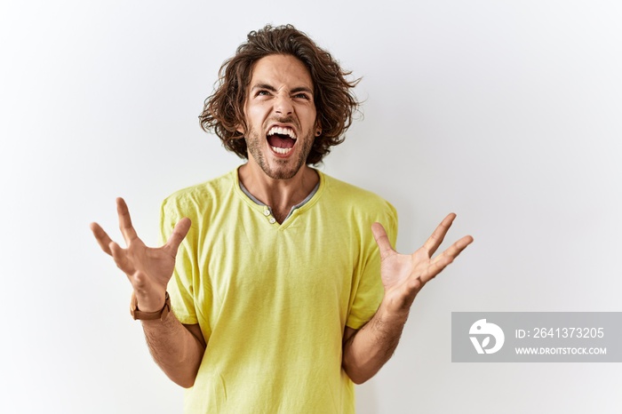 Young hispanic man standing over isolated background crazy and mad shouting and yelling with aggress