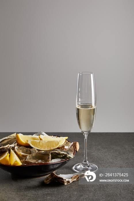 delicious oysters and lemons in bowl with ice near champagne glass with sparkling wine isolated on g