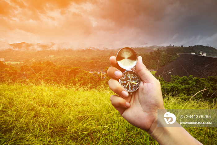 Hand holding a compass on nature background.