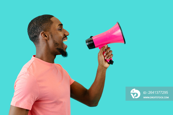 Portrait of a smiling young man speaking through megaphone with mouth open