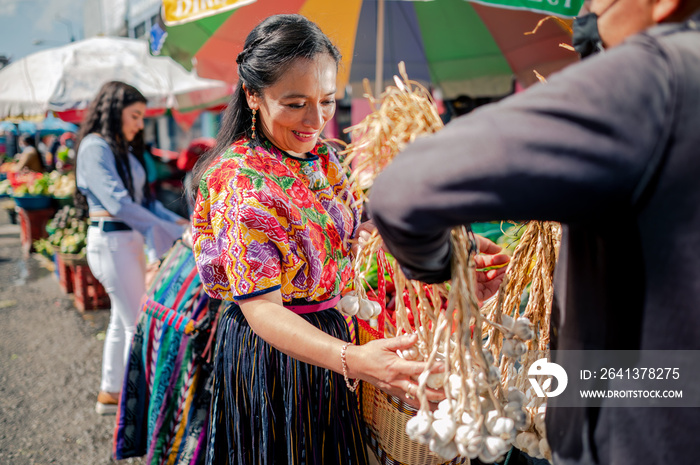 Mujer guatemalteca comprando ajos a un vendedor de un mercado local.