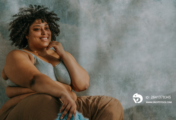 portrait of a plus size afro indigenous person sitting with hand on face and smiling