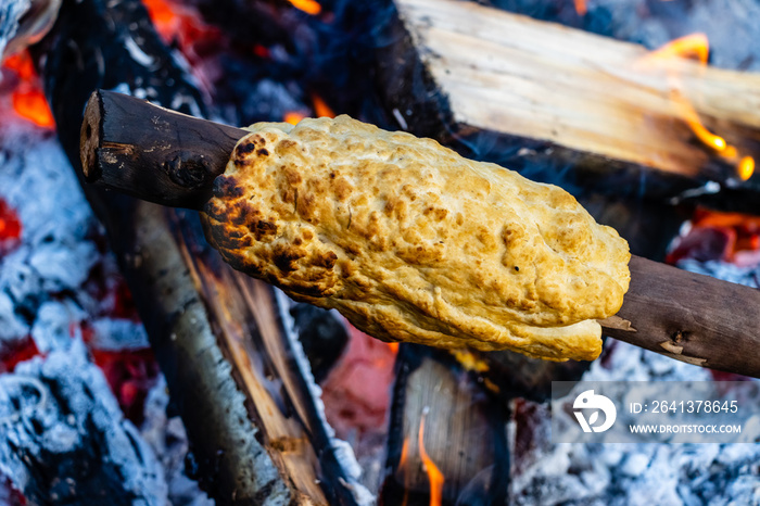 Bannock being cooked traditionally over an open fire on a stick