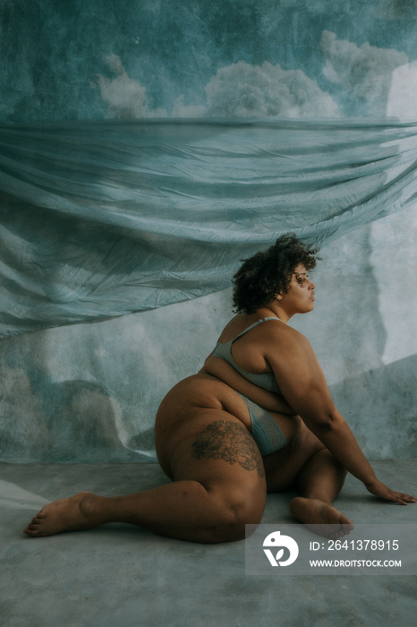 portrait of a plus size afro indigenous person sitting on floor looking towards the sun