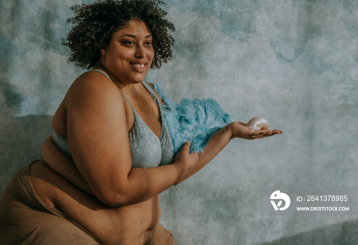 portrait of a plus size afro indigenous non binary person holding feathers and a seashell